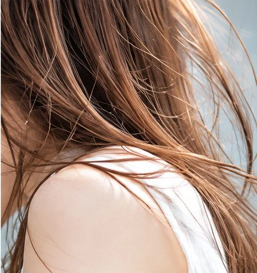 風になびく茶色のロングヘアと、白い服の肩のクローズアップ